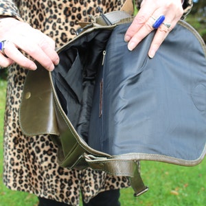 May include: A green leather satchel bag with a black fabric lining. The bag has a flap closure and a buckle strap. The bag is open and the lining is visible.