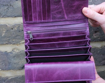Könnte beinhalten: Eine tiefviolette Geldbörse aus Leder mit einem Akkordeon-Design mit mehreren Fächern. Das Innere umfasst mehrere vertikale Kartenfächer, ein Reißverschlussfach und verschiedene offene Bereiche, die alle mit einem Druckknopf verschlossen werden.