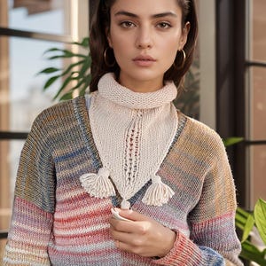 Può includere: Una donna indossa un maglione a righe multicolori con una sciarpa di uncinetto bianca e jeans blu.