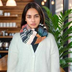 May include: A woman wearing a white cardigan with a colorful striped infinity scarf. The scarf has shades of red, orange, blue, green, black, white, and pink.