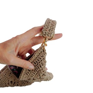May include: A beige crocheted handbag with a gold clasp and a crocheted strap. The bag is being held by a hand.