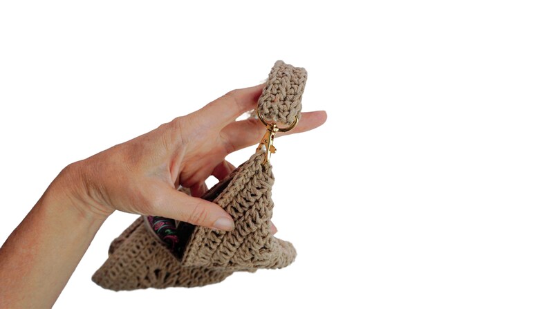 May include: A beige crocheted handbag with a gold clasp and a crocheted strap. The bag is being held by a hand.