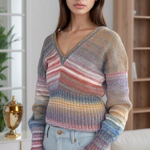 Peut inclure: Une femme portant un pull rayé multicolore avec un col en V et des manches longues. Elle porte un jean bleu clair.