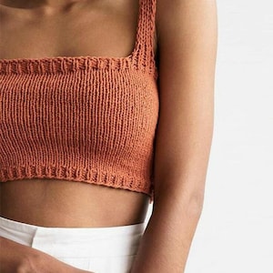 May include: A close-up of a burnt orange knitted crop top with a square neckline and thin straps.