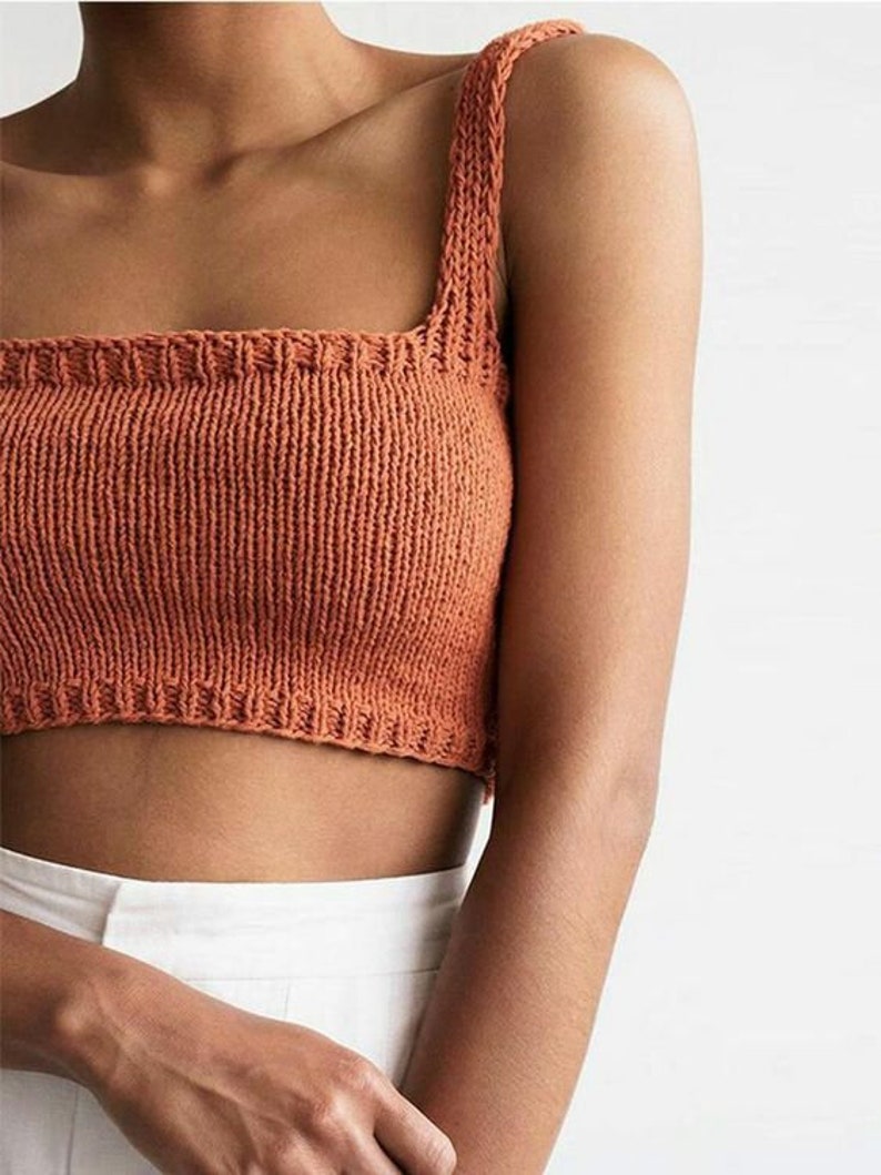 May include: A close-up of a burnt orange knitted crop top with a square neckline and thin straps.