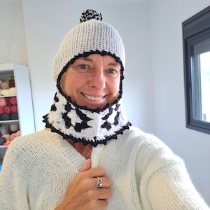 May include: A white knitted hat with a black pom pom and a black and white crocheted neck warmer.