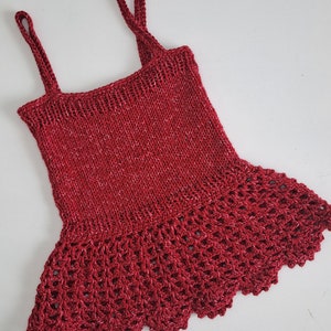 May include: A red knitted sleeveless top with a crocheted lace trim around the bottom.
