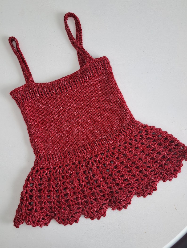 May include: A red knitted sleeveless top with a crocheted lace trim around the bottom.