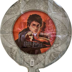 Può includere: Un palloncino rotondo argentato con un designo grigio e bianco. Il centro del palloncino presenta un cerchio rosso con un'immagine di Harry Potter che tiene una bacchetta magica. Il testo "Harry Potter" è stampato sotto l'immagine.
