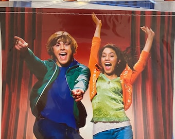 May include: High School Musical birthday banner featuring a blue banner with the words "Happy Birthday" in yellow letters. The banner is 8.42 feet long. The banner features a photo of two people jumping in front of a red curtain.