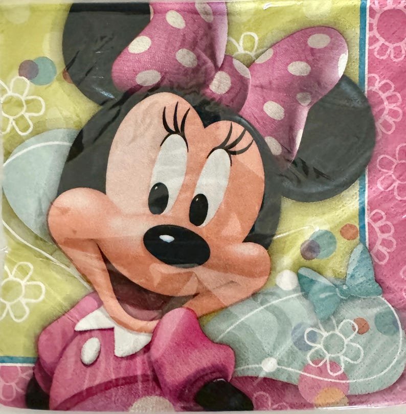 May include: A pink and yellow party napkin with a cartoon image of Minnie Mouse. Minnie Mouse is wearing a pink dress with white polka dots and a pink bow with white polka dots.