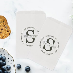 May include: Two white paper bags with a personalised logo featuring the letter "S" and the text "The Sampleton. Kelly & John. The Sampleton."