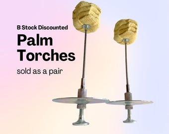 May include: Two palm torches with yellow woven heads, metal stems, and silver-colored bases. The text on the image reads "B Stock Discounted Palm Torches sold as a pair."