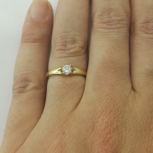 May include: A simple gold band ring with a single, small, round diamond.