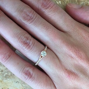 May include: A rose gold engagement ring with a round center stone and smaller stones set in the band.