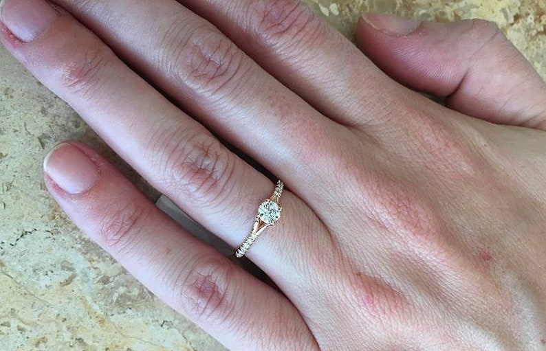 May include: A rose gold engagement ring with a round center stone and smaller stones set in the band.