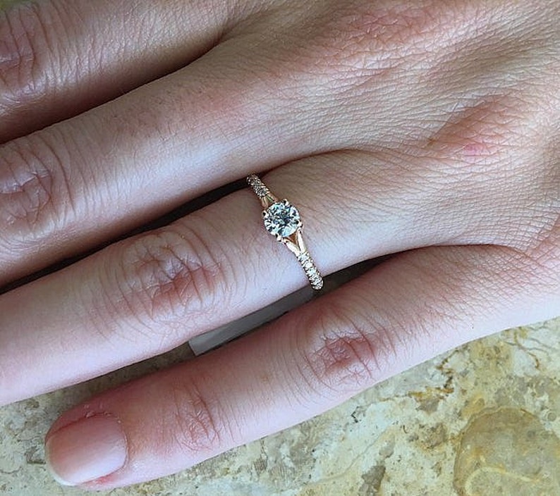 May include: A rose gold engagement ring with a single round diamond set in a prong setting. The band is adorned with small diamonds.