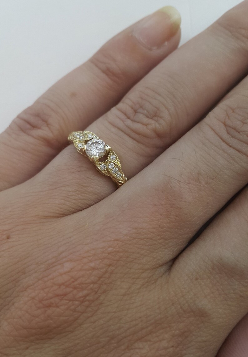 May include: A gold ring with a single round diamond set in a leaf-shaped design. The ring is set with smaller diamonds around the center stone.