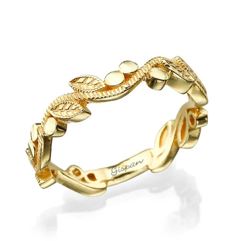 May include: A delicate gold band ring with a leaf and vine design. The ring is inscribed with the word "Gispan".