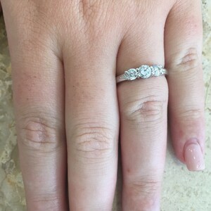 May include: A silver band with three round diamonds set in a row. The diamonds are clear and sparkly.
