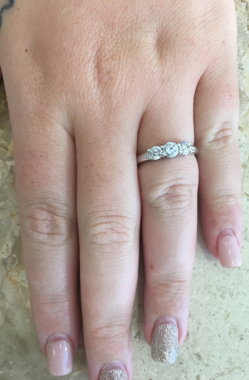 May include: A silver band with three round diamonds set in a row. The diamonds are clear and sparkly.