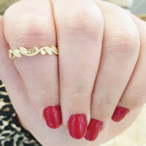 May include: A delicate gold ring with a leaf and flower design. The ring is on a finger with red nail polish.