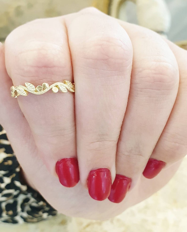 May include: A delicate gold ring with a leaf and flower design. The ring is on a finger with red nail polish.