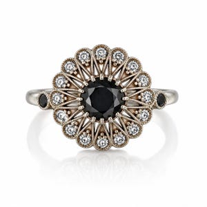 May include: A silver ring with a large black center stone, surrounded by a halo of smaller white stones and a decorative filigree design. Two small black stones are set on either side of the ring's band. The ring has a vintage or antique aesthetic.