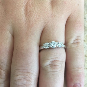 May include: A silver ring with three round diamonds set in a row. The centre diamond is larger than the two diamonds on either side.
