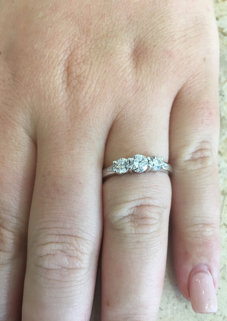 May include: A silver ring with three round diamonds set in a row. The centre diamond is larger than the two diamonds on either side.