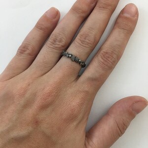 May include: A silver band ring with a delicate design of leaves and small clear stones.