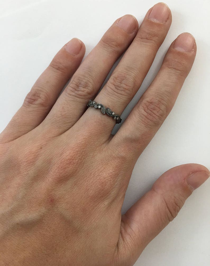 May include: A silver band ring with a delicate design of leaves and small clear stones.