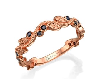 Op de afbeelding: Een roségouden bandring met een delicaat bladontwerp en zwarte saffieren. De ring is gegraveerd met het woord "Gispan".