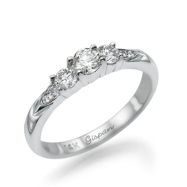 May include: A silver ring with three round diamonds set in a row. The ring is engraved with "14K Gisman" on the inside band.