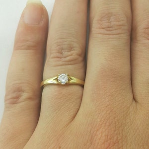 May include: A gold band ring with a single round diamond in the center.