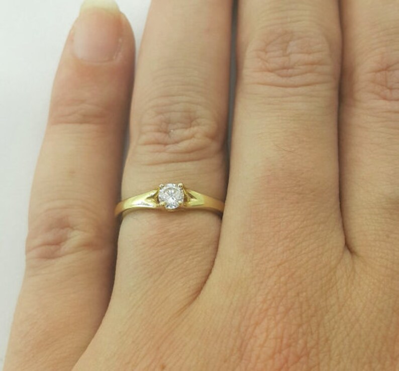May include: A gold band ring with a single round diamond in the center.