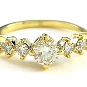 May include: A gold band ring with a large, clear, round-cut center stone and smaller, clear, round-cut stones on either side. The ring is set in a prong setting.