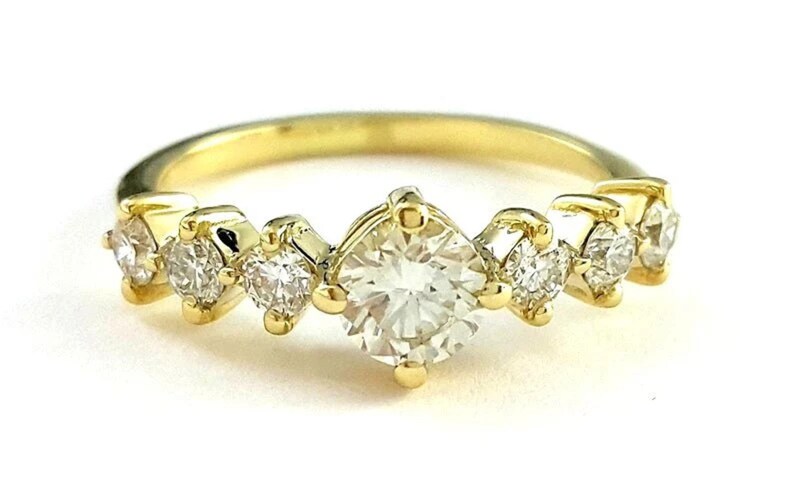 May include: A gold band ring with a large, clear, round-cut center stone and smaller, clear, round-cut stones on either side. The ring is set in a prong setting.
