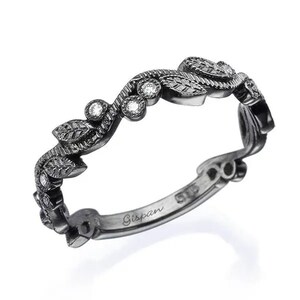 May include: Black band ring with a delicate leaf design and small diamonds. The ring is engraved with the word "Gispan" on the inside.