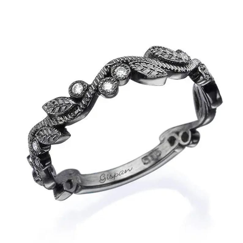 May include: Black band ring with a delicate leaf design and small diamonds. The ring is engraved with the word "Gispan" on the inside.