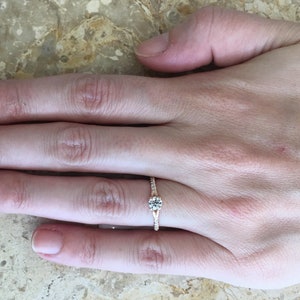 May include: A rose gold engagement ring with a single round diamond and smaller diamonds set in the band.