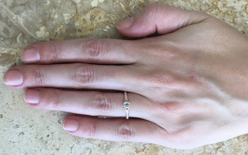 May include: A rose gold engagement ring with a single round diamond and smaller diamonds set in the band.