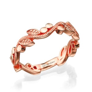 May include: A rose gold band ring with a delicate leaf design. The ring is engraved with the word "Gispan".