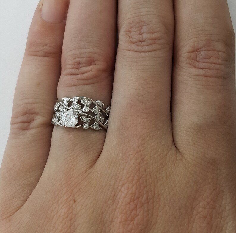 May include: A silver ring with a large, round, clear gemstone surrounded by smaller gemstones. The ring is set in a delicate, leaf-like design.