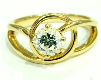 Op de afbeelding: Een gouden ring met een enkele, ronde, heldere steen in een gedraaide band.