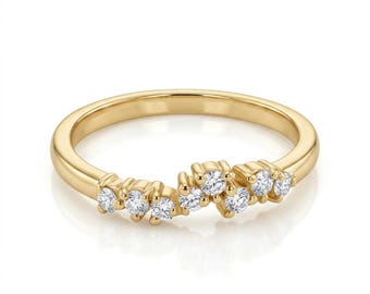 May include: A polished yellow gold ring featuring a curved, asymmetrical cluster of seven round, clear, faceted stones set along the top portion of the band. The metal has a smooth, reflective finish, and the stones are arranged in a staggered pattern.