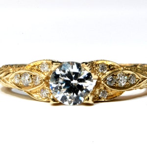May include: A gold ring with a large, round, clear diamond in the center. The ring is decorated with smaller diamonds and a leaf design.