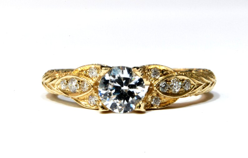 May include: A gold ring with a large, round, clear diamond in the center. The ring is decorated with smaller diamonds and a leaf design.