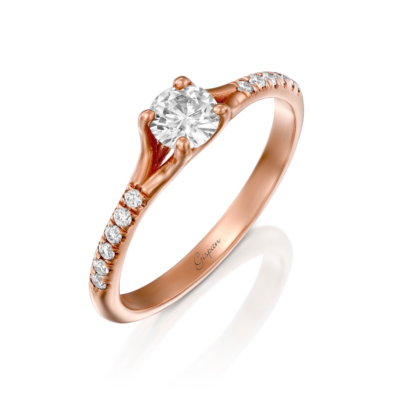 May include: A rose gold engagement ring with a single round diamond and a band of smaller diamonds. The ring is engraved with the word "Gispen".