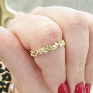 May include: A delicate gold ring with a leaf and flower design. The ring is on a finger with red nail polish.